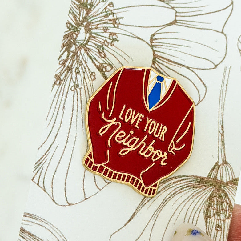 Pin with red sweater design and 'Love Your Neighbor' text on a floral background